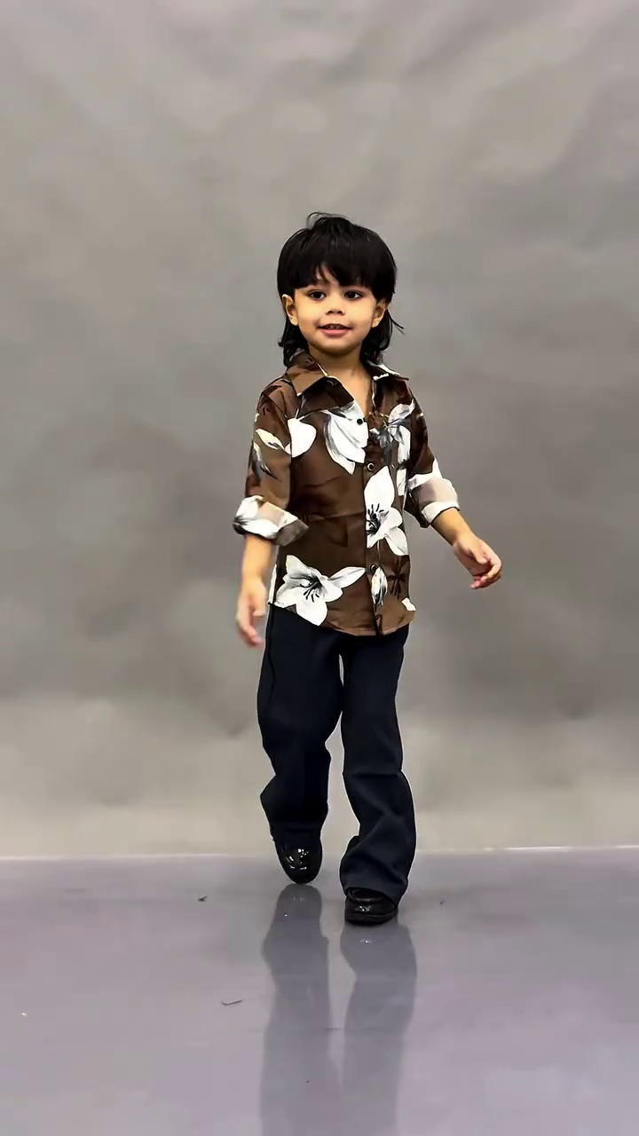 This image shows a young child wearing a fashionable black floral print shirt paired with dark trousers.