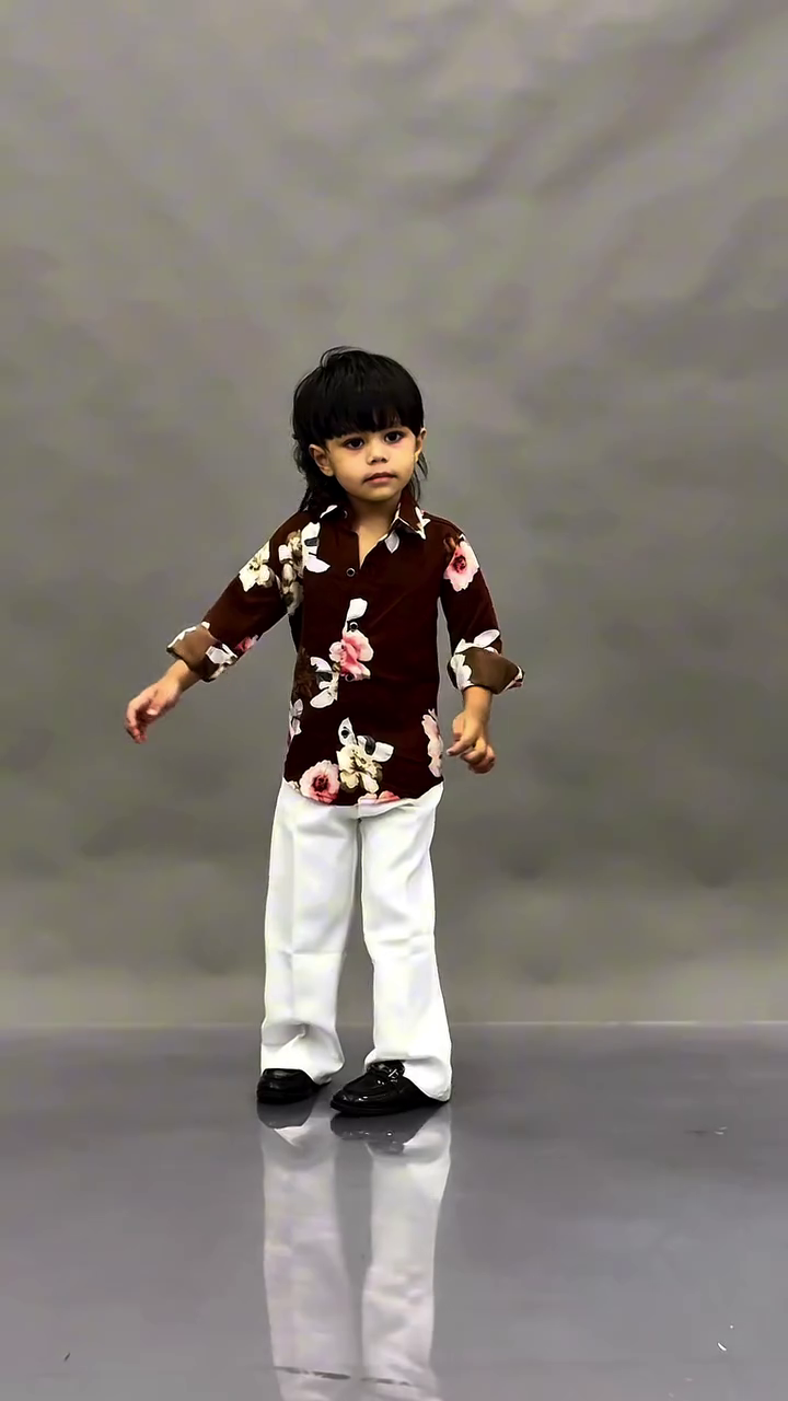 This image shows a young child wearing a fashionable black floral print shirt paired with dark trousers.