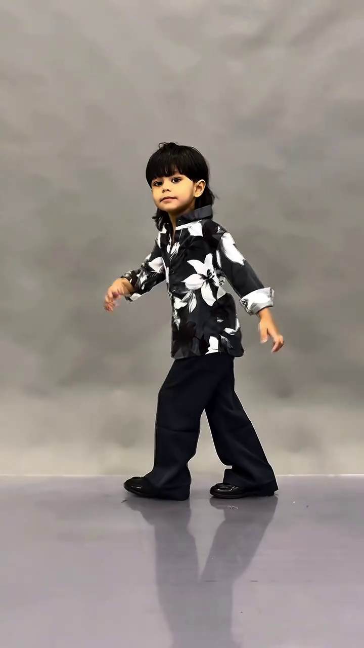 This image shows a young child wearing a fashionable black floral print shirt paired with dark trousers.