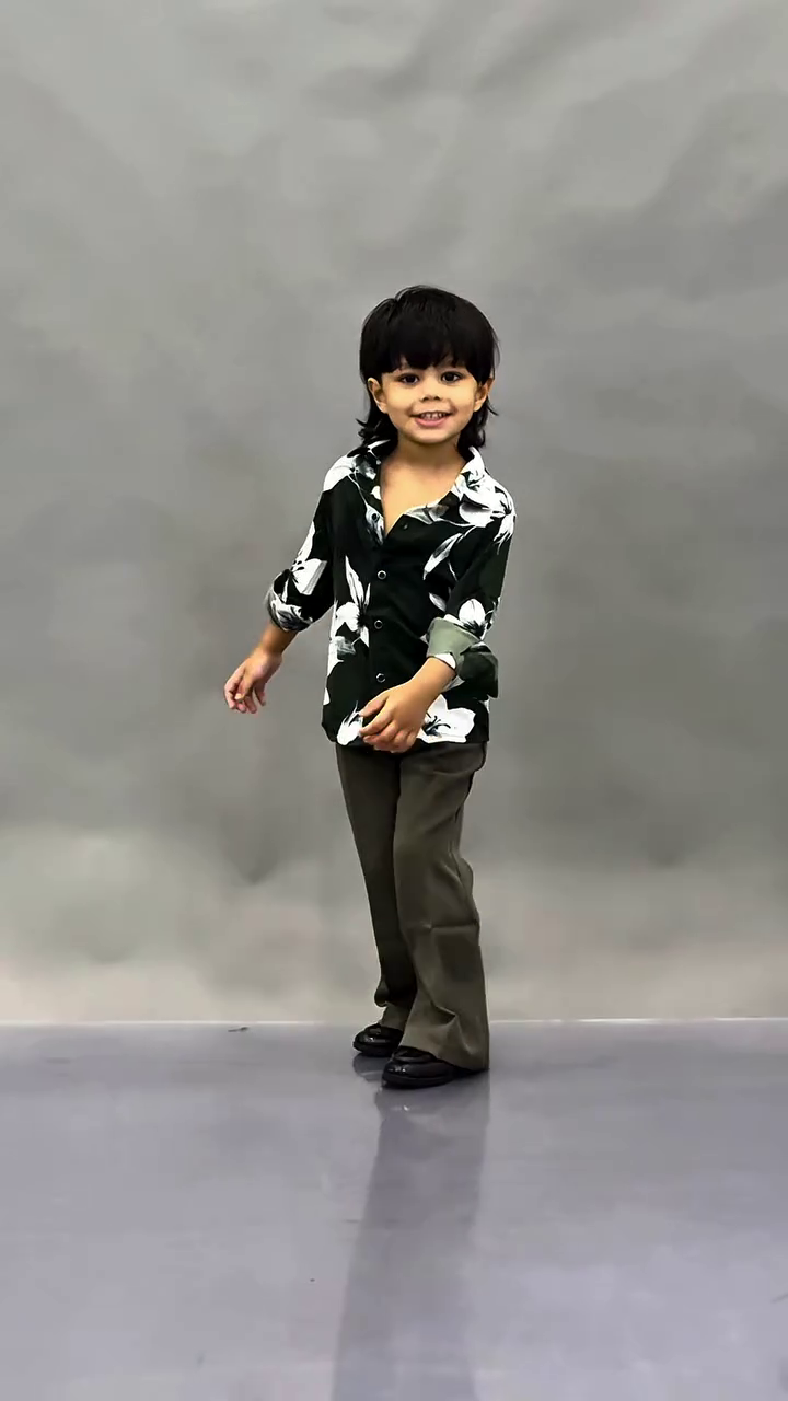 This image shows a young child wearing a fashionable black floral print shirt paired with dark trousers.